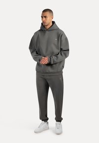 Mørkegrå hættetrøje med oversized pasform, frontlomme og ribbede manchetter. Kombineret med matchende joggers og hvide sneakers. Glat stoftekstur.