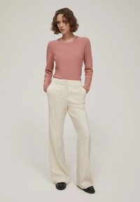 Maglione rosa chiaro e pantaloni a gamba larga color crema. L'outfit presenta texture morbide e un design semplice, abbinato a scarpe nere.