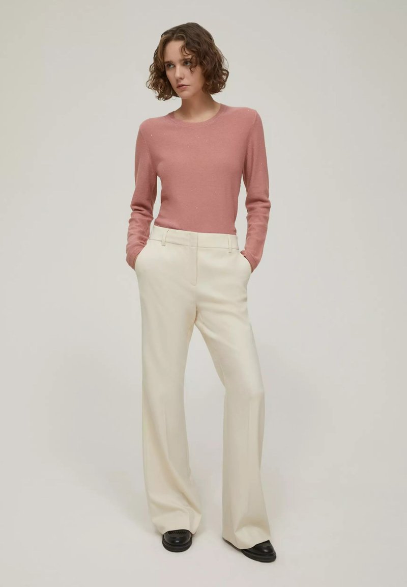 Maglione rosa chiaro e pantaloni a gamba larga color crema. L'outfit presenta texture morbide e un design semplice, abbinato a scarpe nere.