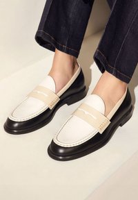 Schwarze und cremefarbene Lederloafers mit gestepptem Design, einem breiten Riemen über dem Spann und einer glatten Oberfläche mit runder Zehenpartie.