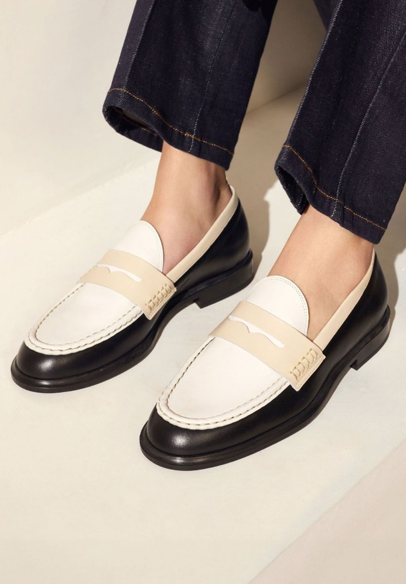 Schwarze und cremefarbene Lederloafers mit gestepptem Design, einem breiten Riemen über dem Spann und einer glatten Oberfläche mit runder Zehenpartie.