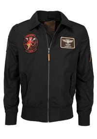 Czarna kurtka bomberka z zapięciem na zamek, prążkowanymi mankietami i kołnierzykiem. Posiada wiele wyszywanych naszywek, w tym logo Top Gun oraz insignia powietrzne.