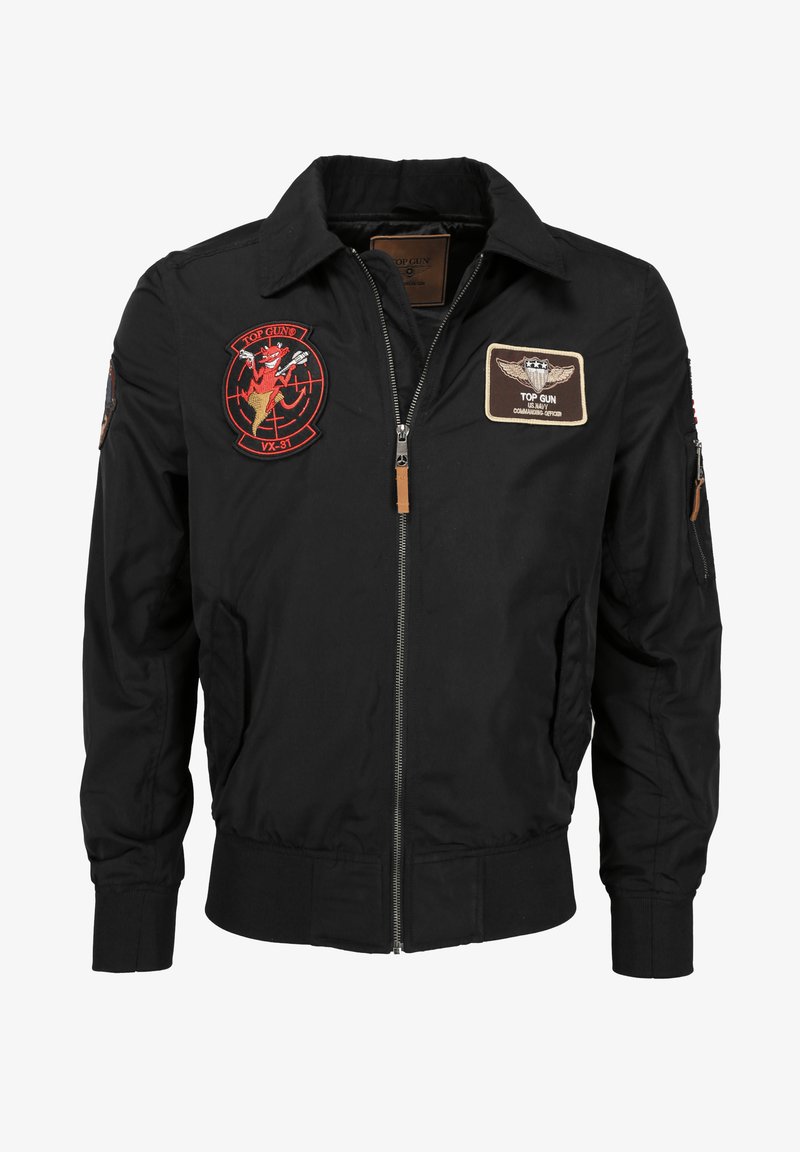 Svart bomberjacka med dragkedja, ribbad mudd och krage. Har flera broderade lappar, inklusive en Top Gun-logotyp och fallskärmsinsignier.