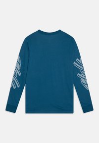 Pitkähihaisen paidan teal-värinen kangas, jossa on rento istuvuus, pyöreä pääntie ja harmaa graafinen kuvio vasemmassa hihassa.