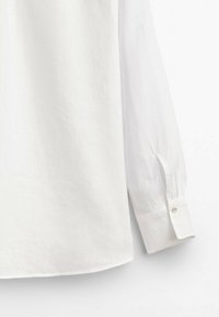 White long-sleeve shirt, cotton blend fabric, with a buttoned cuff and a rounded hem. Features subtle texture and a classic collar design.