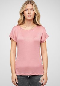 Roza majica s kratkimi rokavi, okroglo izrezana, mehka tekstura in sproščen kroj. V kombinaciji z raztrganimi sivi jeans hlačami z minimalnimi detajli.