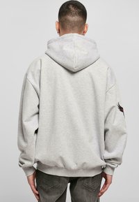 Sweatshirt à capuche gris avec une coupe décontractée, des poignets et un ourlet côtelés. Présente un design d'aile rouge et noir sur la manche gauche.