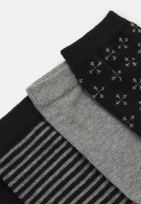 Tres pares de calcetines: uno negro con pequeños patrones blancos, uno gris sólido y uno a rayas en negro y gris. Tejido suave, de punto, con texturas variadas.