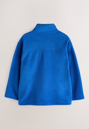 Sininen fleeceneule, jossa on puolikorkea kaulus, pitkät hihat ja sileä pinta. Selässä ja helmassa näkyvät ompelusaumat.