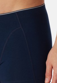 Marineblauwe sportshorts van stof met een gladde textuur, voorzien van platte naden en een contrasterende tailleband met een dunne, lichte streep.