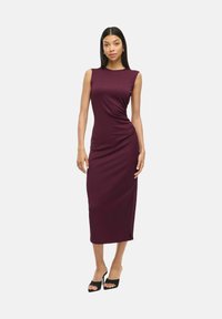 Mauve mouwloze jurk tot op de knie met gedraaide detail op de taille, gemaakt van een gladde stof. Gepaard met zwarte open teen hakken.