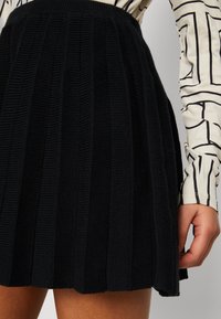 Svart stickad plisserad kjol med en texturerad yta och hög midja, som visar upp vertikala ribbade mönster och en utsvängd form.