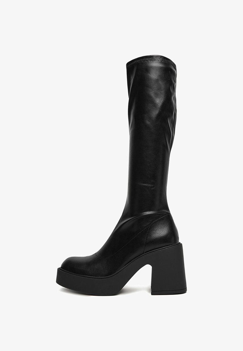 Cizme negre până la genunchi din piele netedă. Au un toc masiv și un vârf rotunjit, cu un brâu ajustat și detalii de coasere minime.