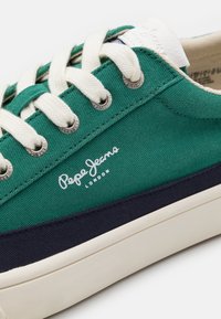 Zelené plátěné tenisky s bílými tkaničkami, námořnickými akcenty a stříbrnými očky. Na boku se nachází logo "Pepe Jeans" v bílé barvě.