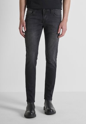 Schmal geschnittene schwarze Jeans aus Denim-Stoff mit glatter Textur, ausgestattet mit Eingrifftaschen und einem dezenten verwaschenen Finish. Kombiniert mit schwarzen Stiefeletten.