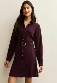 Vestito camicia bordeaux con tessuto strutturato, bottoni sul davanti e maniche lunghe. Dotato di cintura in vita con fibbia color oro.