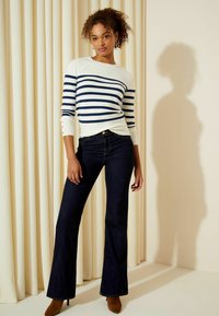 Maglione a righe in bianco e blu navy, con dettagli a bottone, abbinato a jeans a zampa d'elefante blu scuro e stivali con tacco marroni.