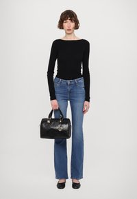 Sac en cuir noir avec une surface texturée, des accents en métal doré et un charme logo rond. Associé à un haut noir ajusté et un jean bleu évasé.