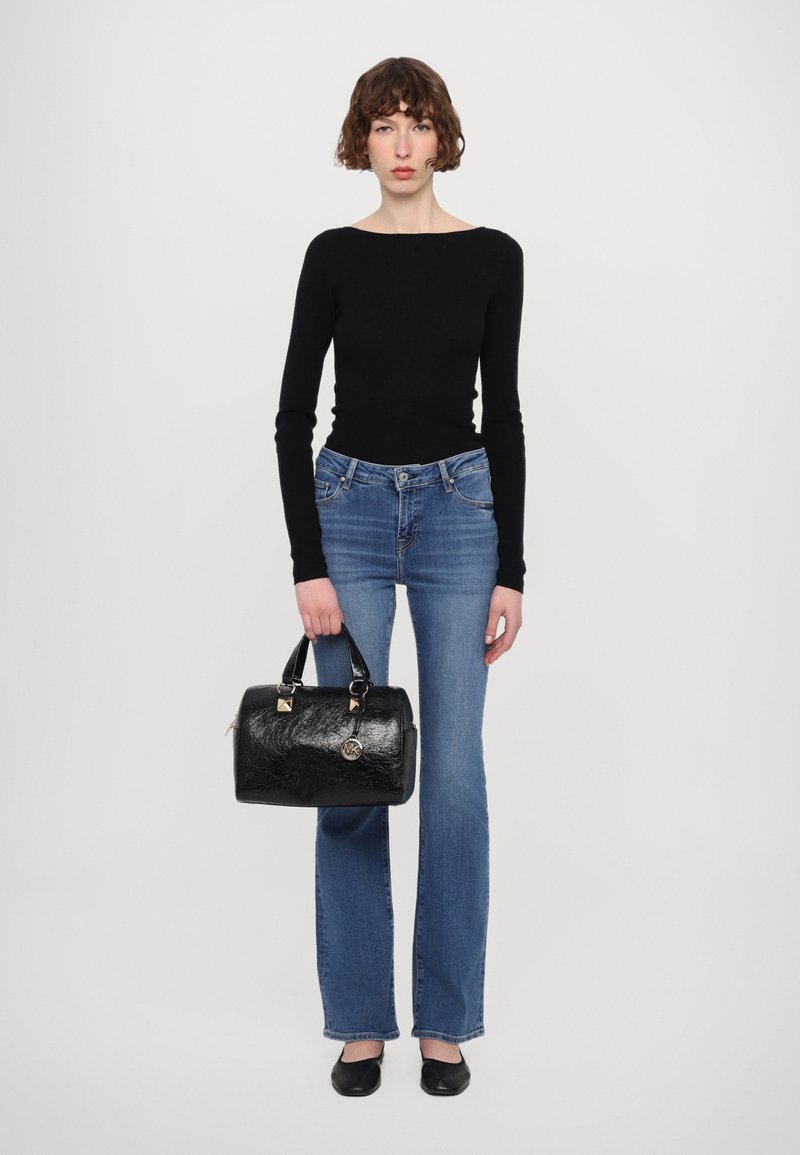 Sac en cuir noir avec une surface texturée, des accents en métal doré et un charme logo rond. Associé à un haut noir ajusté et un jean bleu évasé.