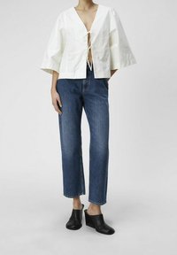 Haut en coton blanc avec un décolleté en V profond et un détail de lien à l'avant ; associé à un jean droit en denim bleu classique et des sabots compensés noirs.