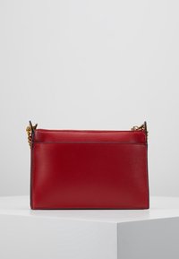 Czerwona skórzana torebka o gładkiej fakturze, prostokątnym kształcie, z zamknięciem na zamek u góry i złotym łańcuszkiem do noszenia.