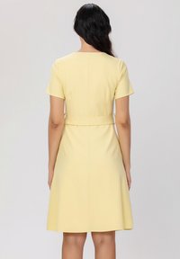 Robe jaune courte avec des manches courtes, taille cintrée et jupe évasée. Tissu lisse et design simple au dos sans fermetures.