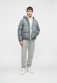 Hallhalline voodriga hall jakk, valge sviiter all, hall spordipüksid ja valged tossud; sile tekstuur ja mugav lõige.