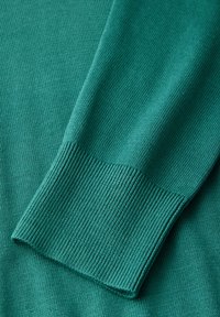 Türkis gestrickter Pullover mit gerippten Bündchen und einer glatten Textur. Nahaufnahme, die sich auf die Stoffdetails und das Ärmeldesign konzentriert.