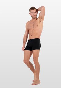Černé bavlněné boxerky s přiléhavým střihem, elastickým pasem a hladkou texturou, které nosí mužský model na neutrálním pozadí.