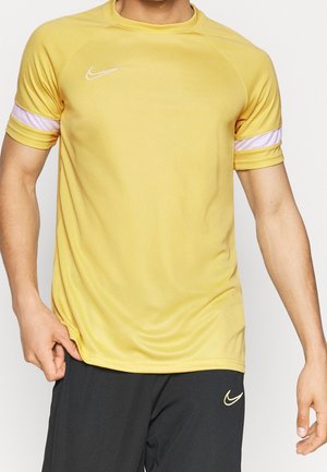 Homme portant un maillot de sport jaune à manches courtes avec une bande blanche sur les manches et un short noir, tous deux avec des logos Nike blancs.