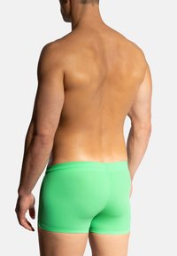 Zelené plavky v těsném střihu, vyrobené z hladkého materiálu, s minimalistickým designem a elastickým pasem, z pohledu zezadu.