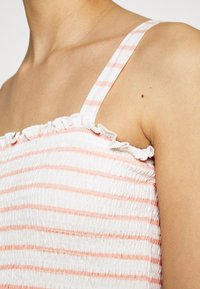 Smockad topp med vita och ljusrosa ränder, med tunna axelremmar och en volangkrage. Slät textur med en figurnära design.