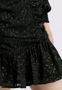 Vestido negro con tejido texturizado, decorado con lentejuelas dispersas, un dobladillo con volantes y un corsé ajustado que se recoge en la cintura.