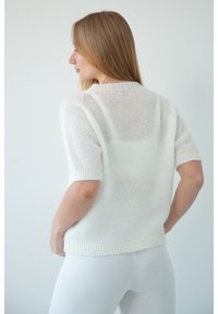 Sweter dzianinowy w miękkim białym kolorze, z krótkimi rękawami, prążkowanym dołem i delikatną, przezroczystą teksturą. Zaprojektowany w luźnym fasonie.