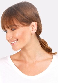Boucles d'oreilles en or porté par une femme aux cheveux bruns, présentant une finition lisse et élégante sur un fond clair.