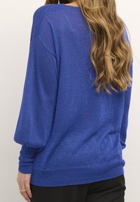 Maglione blu fit morbido con una finitura testurizzata e lucida. Presenta un ampio scollo, spalle cadenti e polsini e orlo a coste.