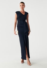 Granatowa, bezrękawnikowa sukienka maxi z marszczeniem w talii oraz rozcięciem do uda. Gładki, połyskujący materiał z delikatnym połyskiem. Srebrne metaliczne sandały.