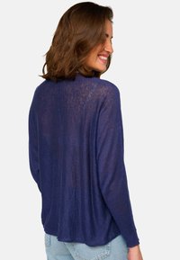 Pull léger bleu marine, à coupe ample, avec des manches longues et une texture légèrement transparente. Doté d'un col rond et d'un détail de couture au dos.