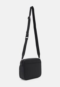 Borsa a tracolla nera realizzata in materiale morbido. Forma rettangolare con chiusura a zip, tracolla regolabile e tasca anteriore per ulteriore spazio di stoccaggio.