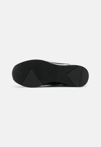 Suola di sneaker nera con texture a righe e modelli angolari. Presenta un fondo piatto con marchio e elementi di trazione distintivi.