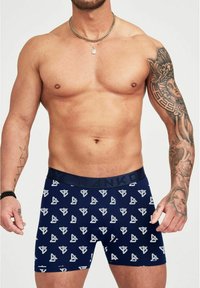 Boxer shorts blu navy con un motivo geometrico bianco ripetuto, elastico in vita e una texture di tessuto morbida. Modello mostrato senza camicia.