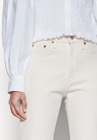 Jeans blancos de cintura alta y corte ajustado, hechos de algodón texturizado, con herrajes de color cobre y cinco bolsillos funcionales.
