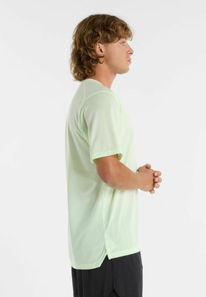 Camiseta atlética verde claro de mangas cortas con tejido texturizado, escote redondo, aberturas laterales y un corte relajado. Llevada con pantalones cortos negros.
