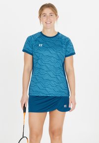 Blå atletisk T-shirt med bølgemønster, korte ærmer og rund hals; parret med en matchende blå nederdel. FZ-logo på begge dele.