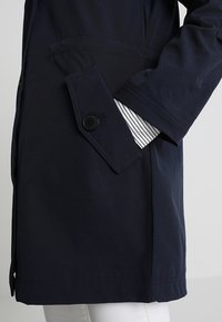 Chaqueta de lluvia azul marino con un bolsillo abotonado y forro interior a rayas. Textura suave y diseño recto, con mangas largas.