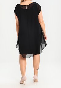 Černé, průsvitné šaty s krátkými rukávy, kulatým výstřihem a detaily v podobě klíčové dírky na zadní straně. Volný silueta a délka po kolena.