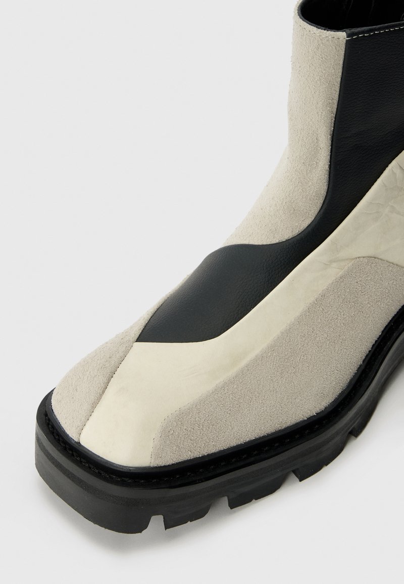 Wildleder- und Leder-Ankle-Boot mit schwarzen und beigen Farbblöcken, einer dicken schwarzen Sohle und einem eleganten Design. Merkmale sind eine glatte Oberfläche und dezente Nähte.