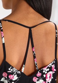 Conception du dos d'une robe noire à fleurs avec des fines bretelles et un motif en croix. Imprimé de fleurs roses et blanches remarquable sur le tissu.