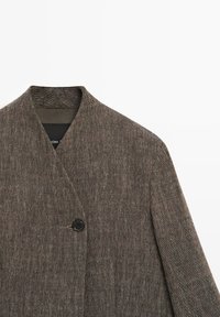 Blazer marron à motif chevrons avec une fermeture à un bouton noir et un col en V sur fond blanc.
