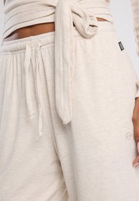 Light beige loungewear set featuring a textured, ribbed fabric with a tie at the waist. Subtle branding displayed on the side of the pants.